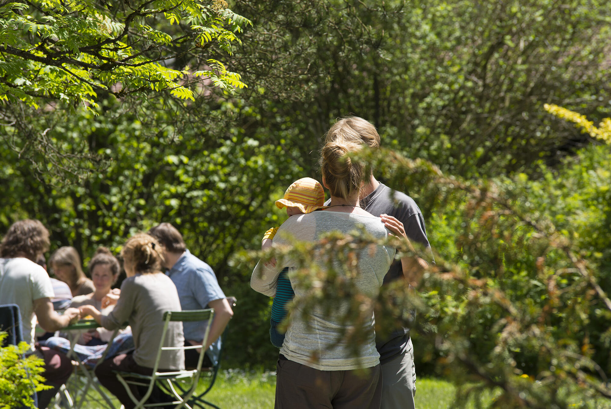 Eine Familie mit Kind im ZIST Garten, während im Hintergrund weitere Menschen sitzen und essen