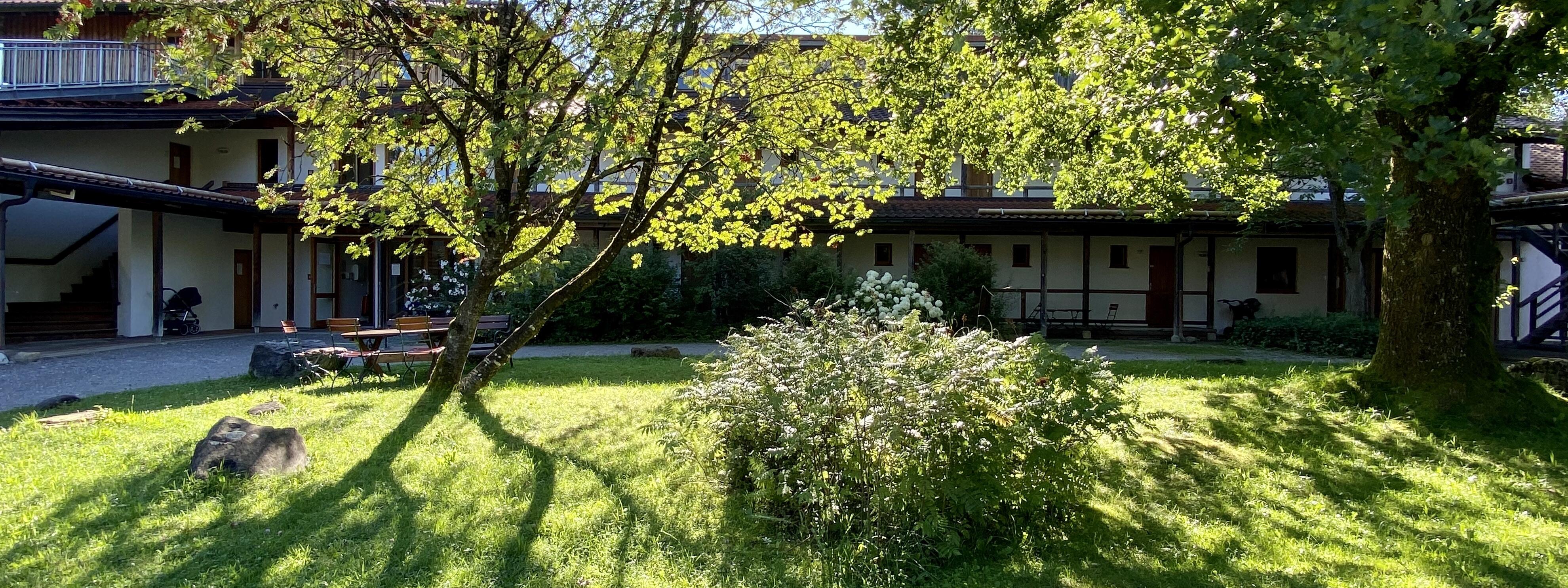 ZIST Innenhof mit Bäumen und Garten, beleuchtet vom Sonnenschein und umgeben vom Seminarhaus.