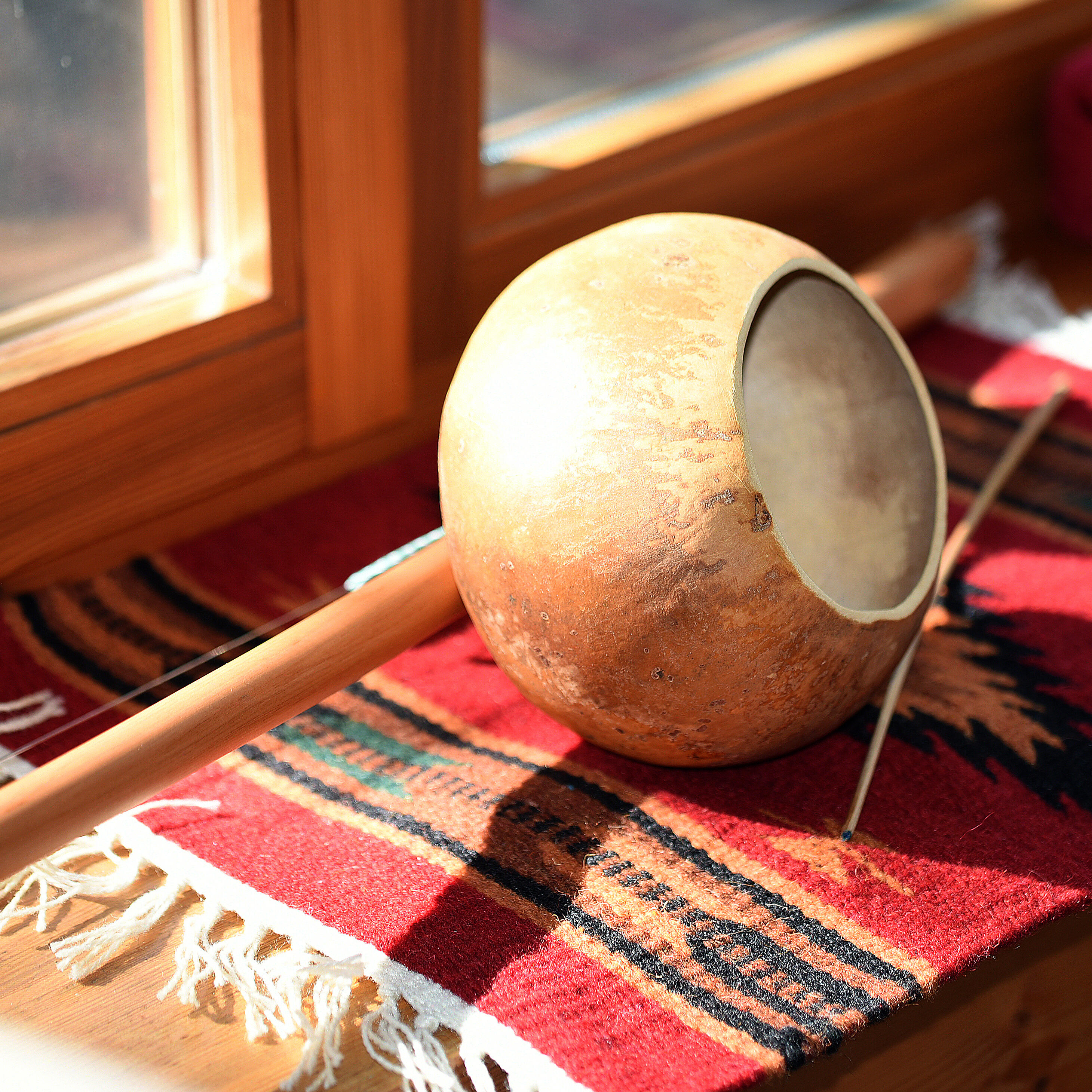 TaKeTiNa | Traditionelles Saiteninstrument mit einem Resonanzkörper aus Kalebasse liegt auf einem kunstvollen, gewebten Teppich im sonnigen ZIST Seminarraum.