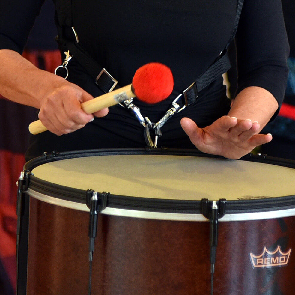 Eine Frau spielt auf einer großen Trommel mit einem roten Schlägel, während die andere Hand den Rhythmus fühlt.