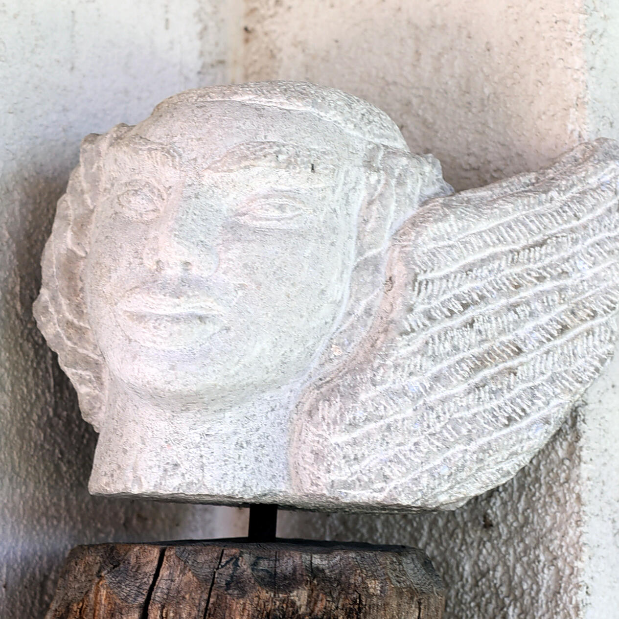 Eine handgefertigte Steinskulptur in ZIST zeigt das Gesicht eines Engels mit detailliert gearbeiteten Flügeln.