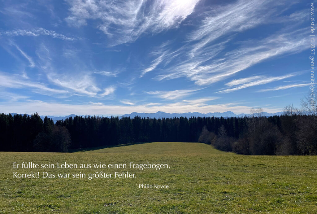 Grüner Hang mit Baumlandschaft am unteren Ende und Blick in die Berge am Horizont, darüber ein strahlend blauer Himmel mit Schleierwolken. An der unteren linken Seite des Bildes in weißer Schrift ein Zitat von Philip Kovce. 