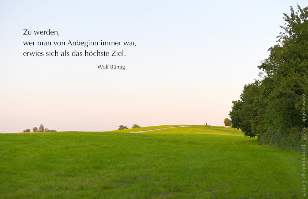 Blick über eine Hügelwiese in das Licht am oberen Ende, rechts eine Baumrguppe, links oben ein Zitat von Wolf Büntig